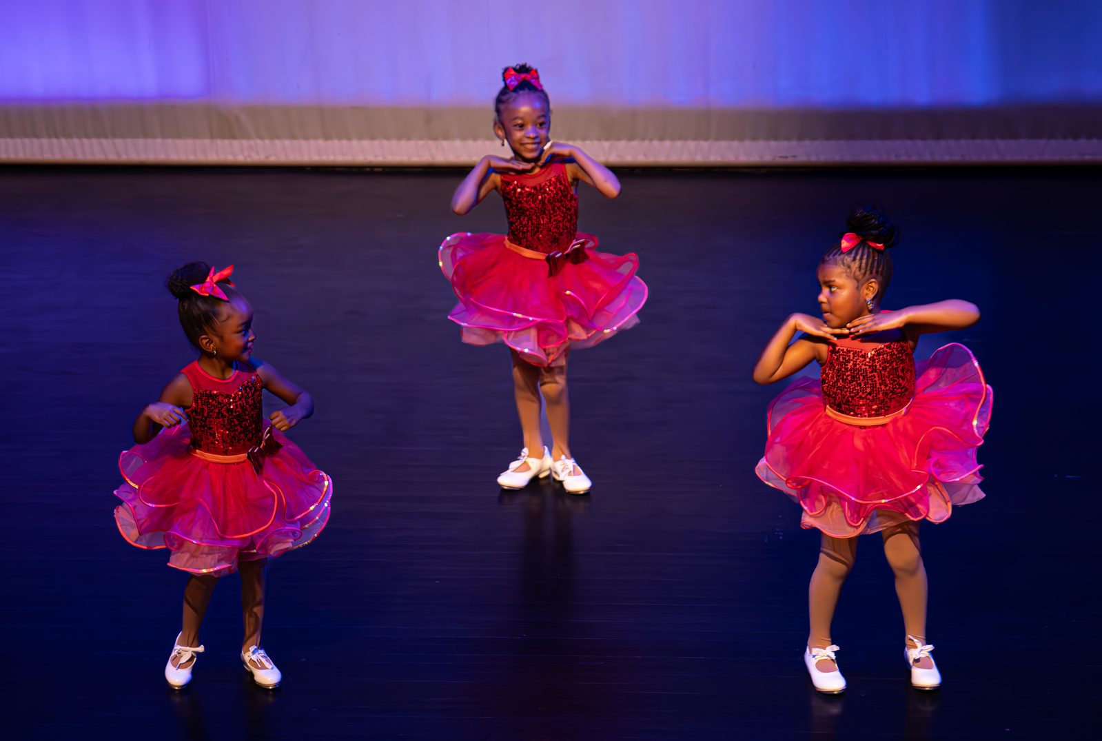 Three young performers in red dresses on stage at the PPR Spring Arts Showcase — click to view gallery